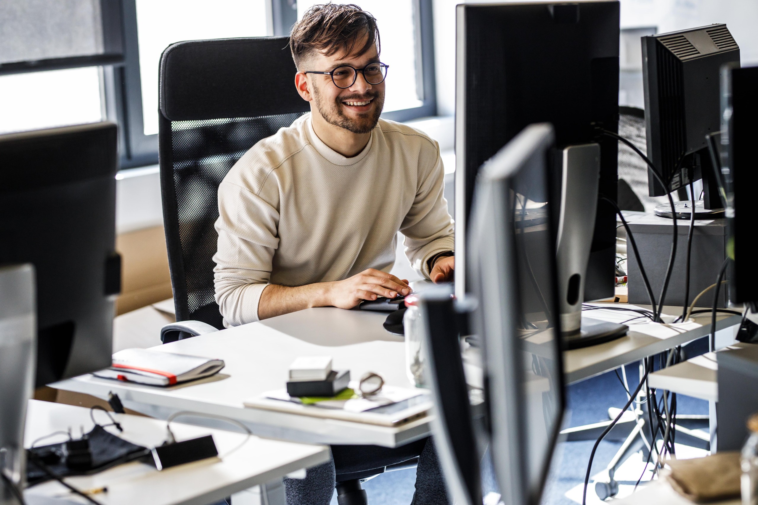 Junger Projektmanager lächelnd vor dem Monitor